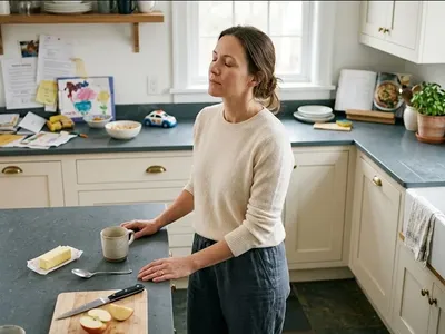 A parent standing in a kitchen surrounded by small unfinished tasks, one hand on the counter, taking a breath, representing the themes of "Getting Diagnosed with ADHD Postpartum: What That Means".