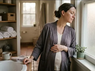 A woman standing near a window, one hand on her belly, soft backlight, representing the themes of "Pregnancy and Parenthood at Advanced Maternal Age: A Mental Health Guide".