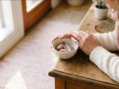 A person at a table with a warm drink, looking forward with a calm, open expression, representing the themes of "The Mental and Emotional Experience of Using Donor Eggs: A Complete Guide".