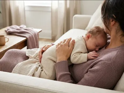 A parent on a couch, infant nestled on their chest, both still and quiet, representing the themes of "Postpartum Sex and Intimacy: Why It Changes and How to Navigate It".